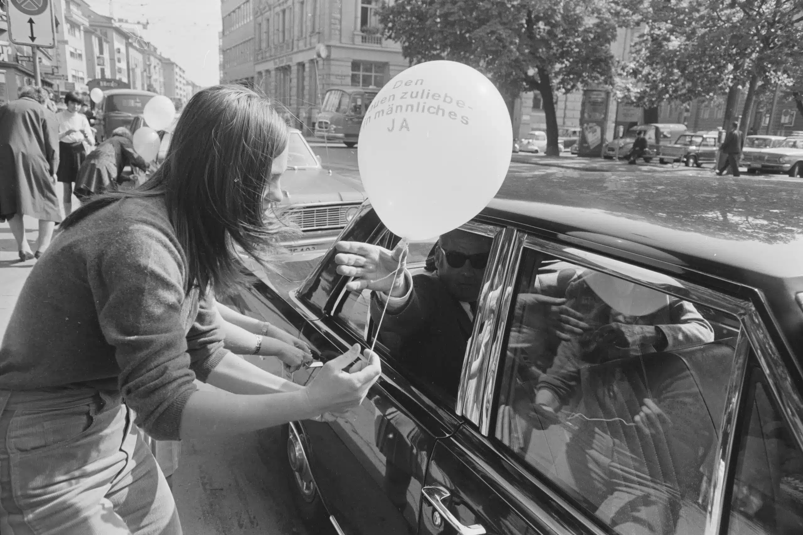 A woman handing a pro-suffrage balloon to a passerby at a protest, Zurich, 1969.